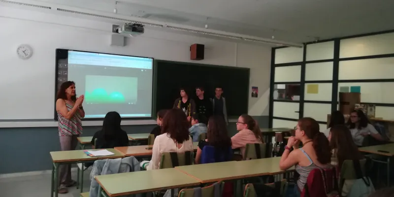 Una aula de secundària. L'alumnat escoltant a la professora amb una pantalla de fons. 